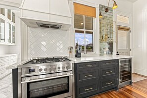 A kitchen with a stainless steel stove, oven, and black cabinetry with gold handles. - Historic Galveston Cottage | Walk to the Beach (Galveston)