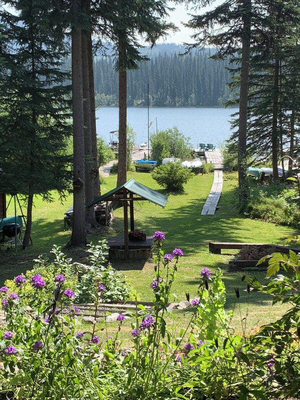 A lakeside cabin with a deck, surrounded by trees and a view of the lake.