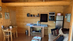 Interior acogedor de una cabaña con una mesa de comedor, un sofá, una pequeña cocina con microondas y tostadora, y un bote de basura.