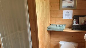 Un baño pequeño de madera con ducha, inodoro y un estante con artículos de tocador.