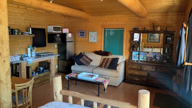Un interior acogedor de cabaña con kitchenette, sofá, mesa de comedor y cama.