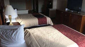 Quarto de hotel com duas camas, uma televisão sobre um suporte e uma luminária.