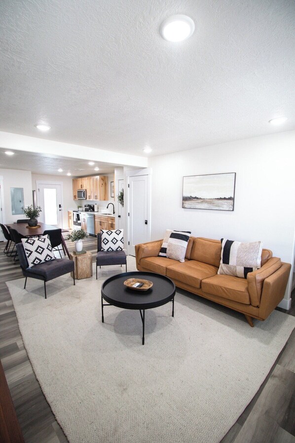 A modern living room with a sofa, two armchairs, a coffee table, and a dining area in the background.