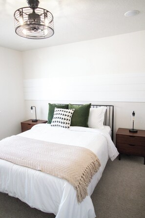 A bedroom with a bed, two bedside tables, a hanging light fixture, and a ceiling light. - The Birch at Creekside Cabins near Lava & Pebble (McCammon)