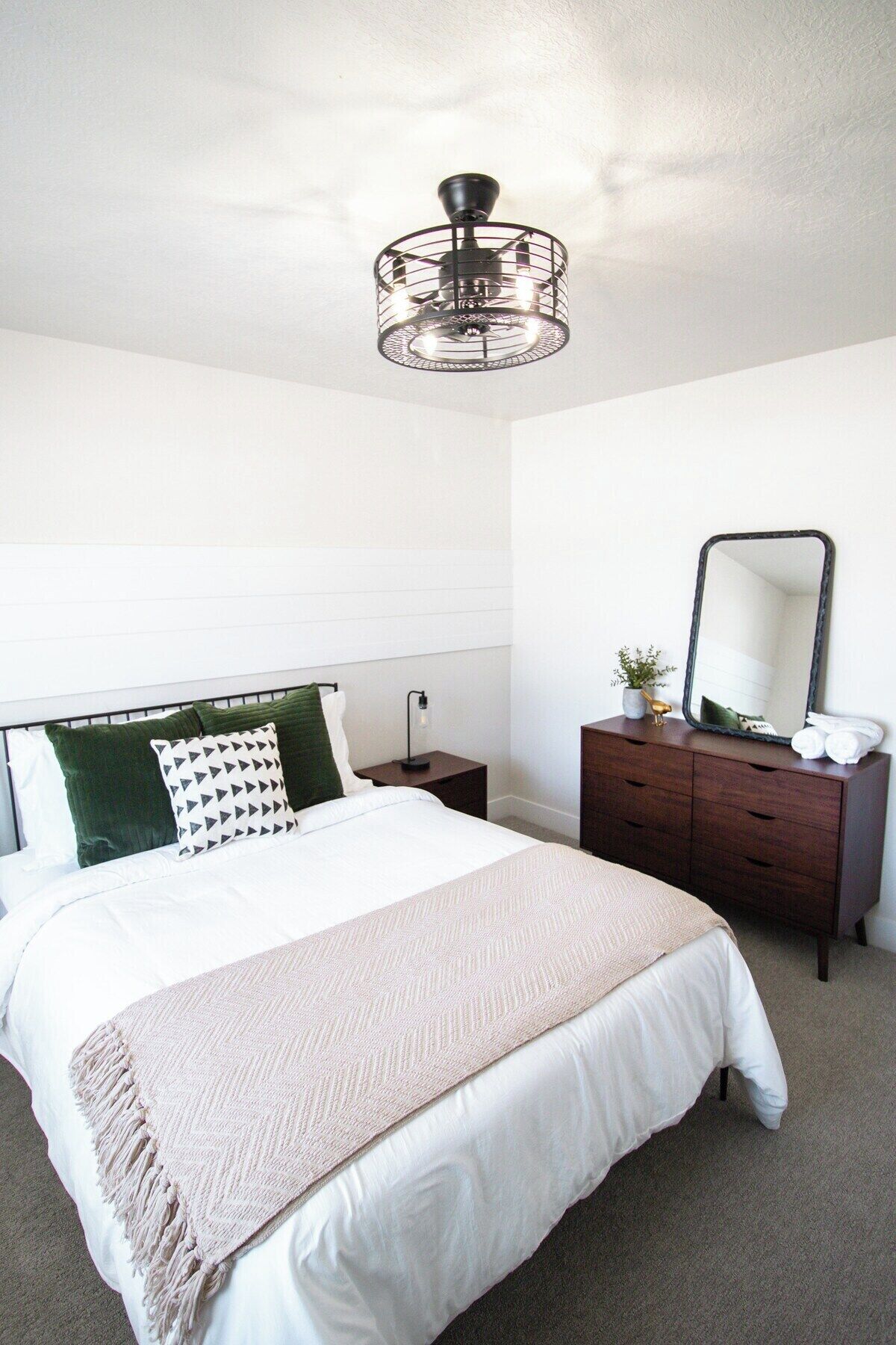 A bedroom with a bed, bedside table, dresser, mirror, and a ceiling light fixture.