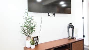 A modern living room with a flat-screen TV mounted on the wall, a wooden entertainment center with a potted plant, and a floor lamp.