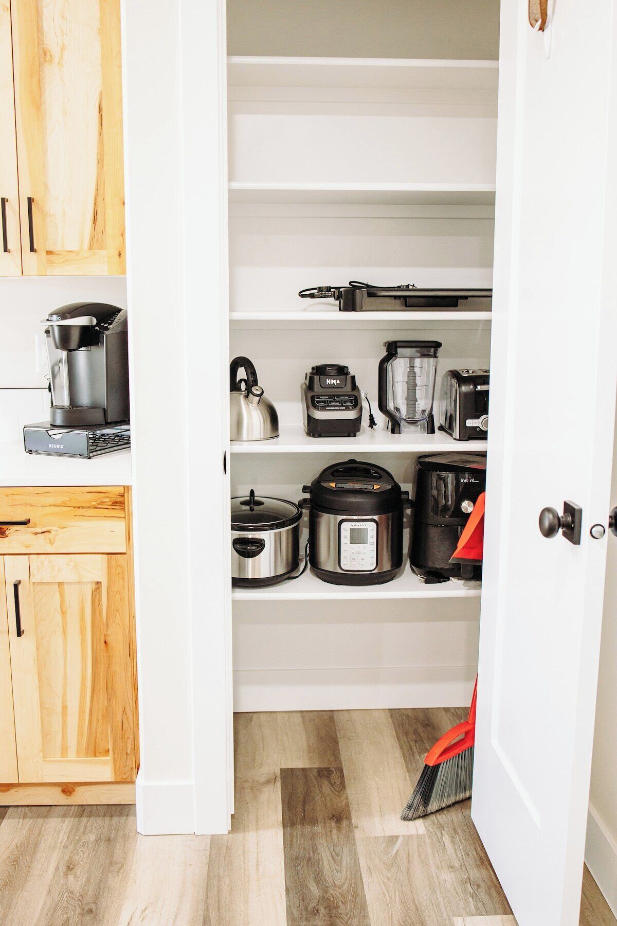 A kitchen with white cabinets and shelves containing various appliances like a coffee maker, kettle, blender, toaster, and slow cooker.
