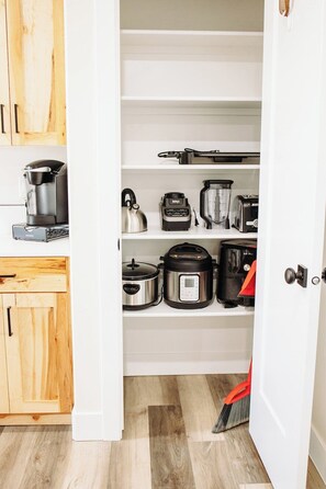 Una cocina con armarios y estantes blancos que contienen varios electrodomésticos como una cafetera, hervidor, licuadora, tostadora y olla de cocción lenta.