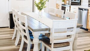 Un comedor con una mesa y sillas de madera, una cocina al fondo y una puerta blanca.