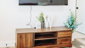Un televisor de pantalla plana montado en la pared sobre un mueble de entretenimiento de madera con una planta y letras decorativas.