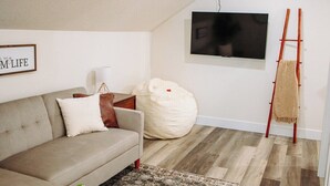 Una sala de estar con un sofá, un televisor montado en la pared, una escalera y un sillón de peluche.