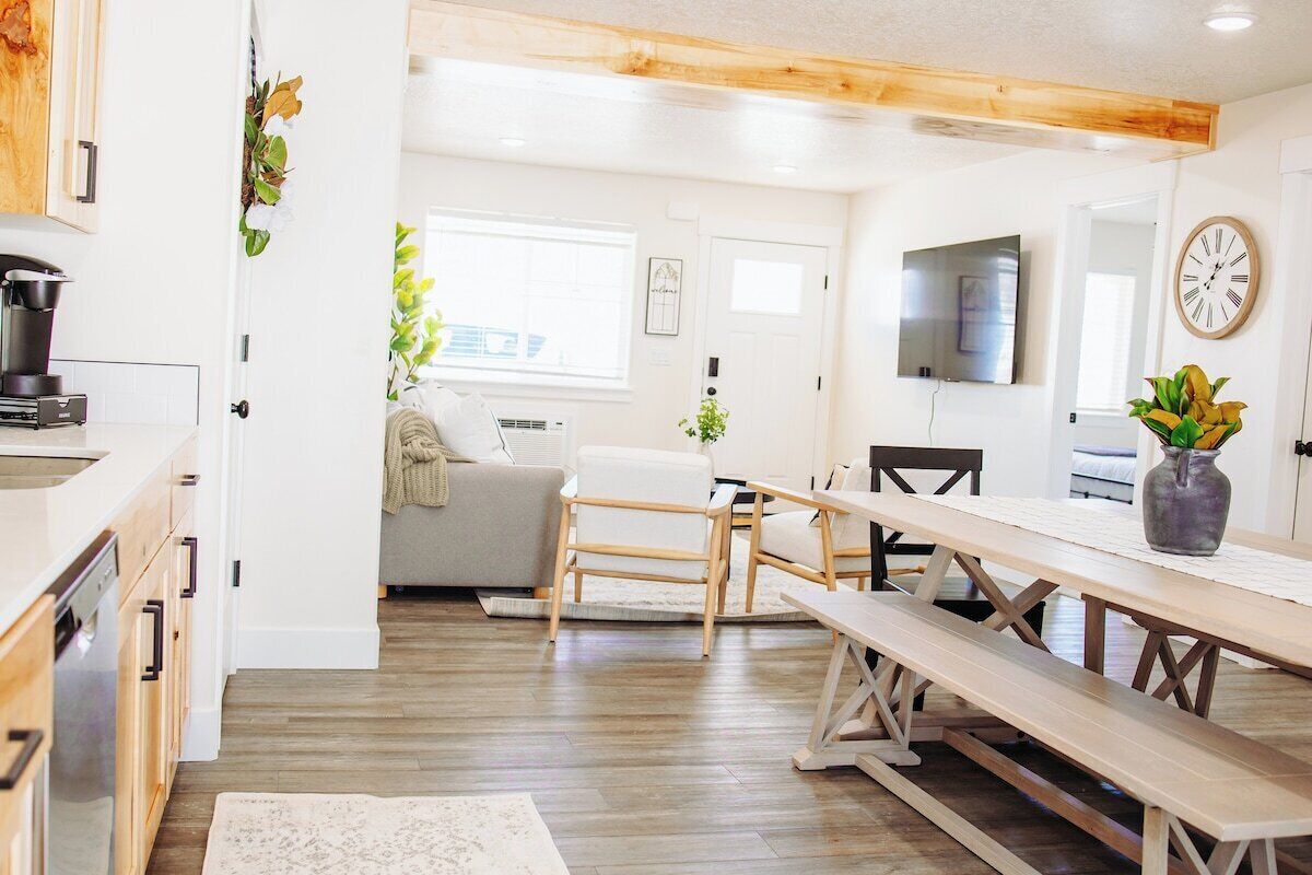 A modern kitchen with wooden cabinets, a dining area with a bench, and a living space with a sofa and a TV.