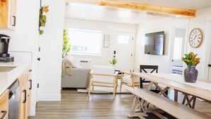 Une cuisine moderne avec des meubles en bois, un coin repas avec un banc et un espace de vie comprenant un canapé et un téléviseur.