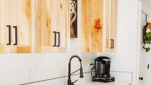 Une cuisine avec des meubles en bois, un plan de travail blanc, un lave-vaisselle en acier inoxydable et une machine à café.