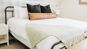 Un lit bien fait, avec une couette blanche, deux oreillers noirs et un oreiller décoratif de couleur beige.