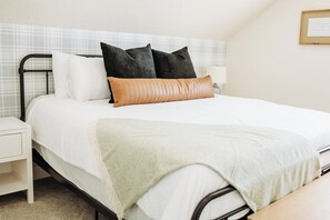 Un lit bien fait, avec une couette blanche, deux oreillers noirs et un oreiller décoratif de couleur beige.