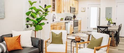 A modern living room with a black sofa, two wooden chairs, a coffee table, and a large green plant.
