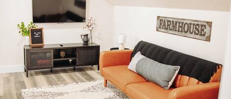 A living room with a television, a sofa, a cabinet, and a wall sign that reads 'FARMHOUSE'.