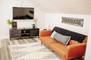 Ein Wohnzimmer mit Fernseher, einer Couch, einem Schrank und einem Wandschild mit der Aufschrift 'FARMHOUSE'.