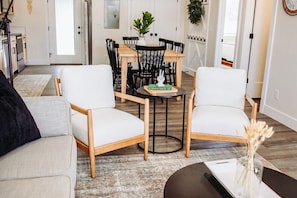 Een moderne woonkamer met een bank, twee fauteuils, een salontafel en een eettafel met stoelen.