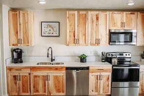 Una cocina con armarios de madera, electrodomésticos de acero inoxidable, lavavajillas y cafetera.