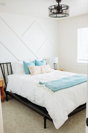 Un dormitorio con cama, mesita de noche, lámpara y ventana.