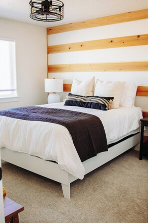 Un dormitorio con cama, mesita de noche, lámpara y cabecero de madera.