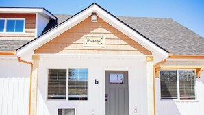 Ein Haus mit einem 'Hickory' Schild über dem Eingang, einer grauen Tür und zwei mit Jalousien versehenen Fenstern.