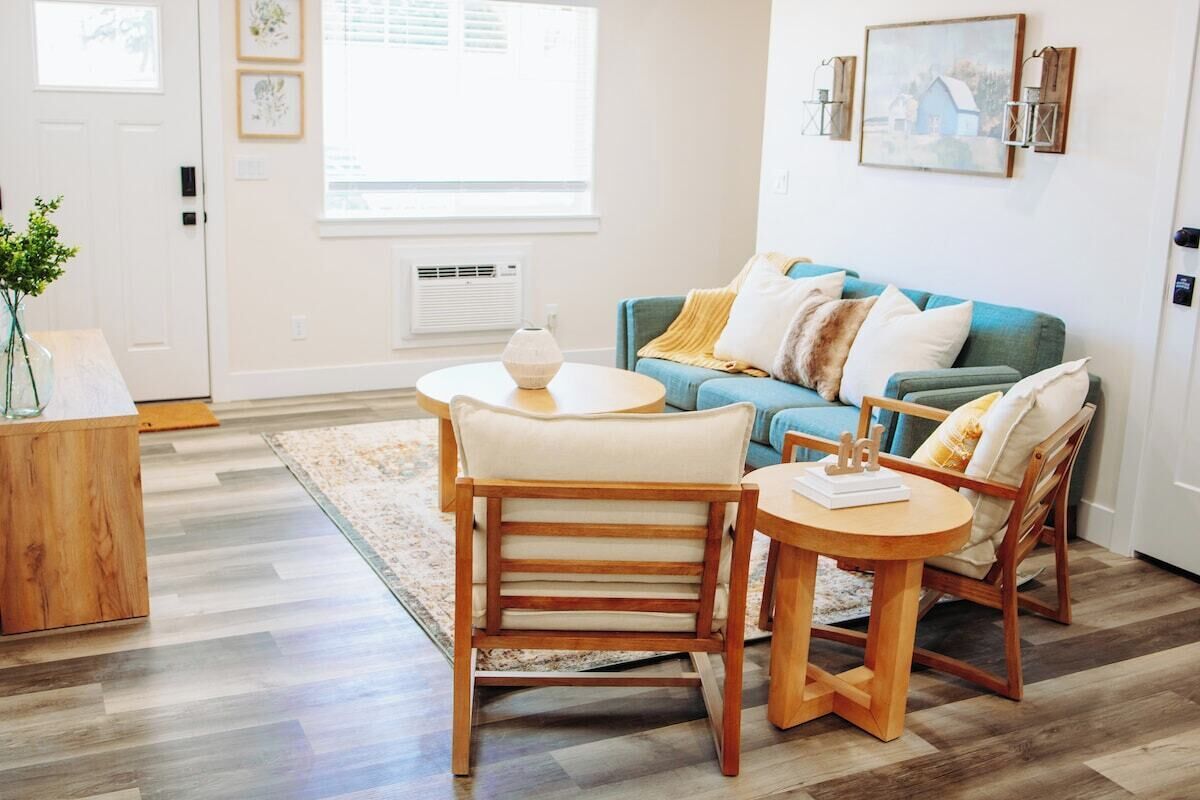 Ein Wohnzimmer mit einem blauen Sofa, zwei Holzstühlen, einem runden Couchtisch und einem Holztisch.