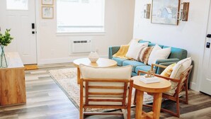 Ein Wohnzimmer mit einem blauen Sofa, zwei Holzstühlen, einem runden Couchtisch und einem Holztisch.