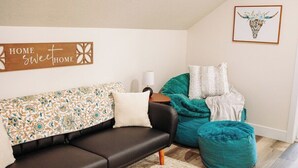 Ein modernes Wohnzimmer mit einem dunkelbraunen Sofa, einem türkisblauen Pouf und einem gemusterten Überwurf.