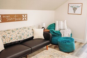 Una sala moderna con un sofá marrón oscuro, un pouf turquesa y un plaid estampado.
