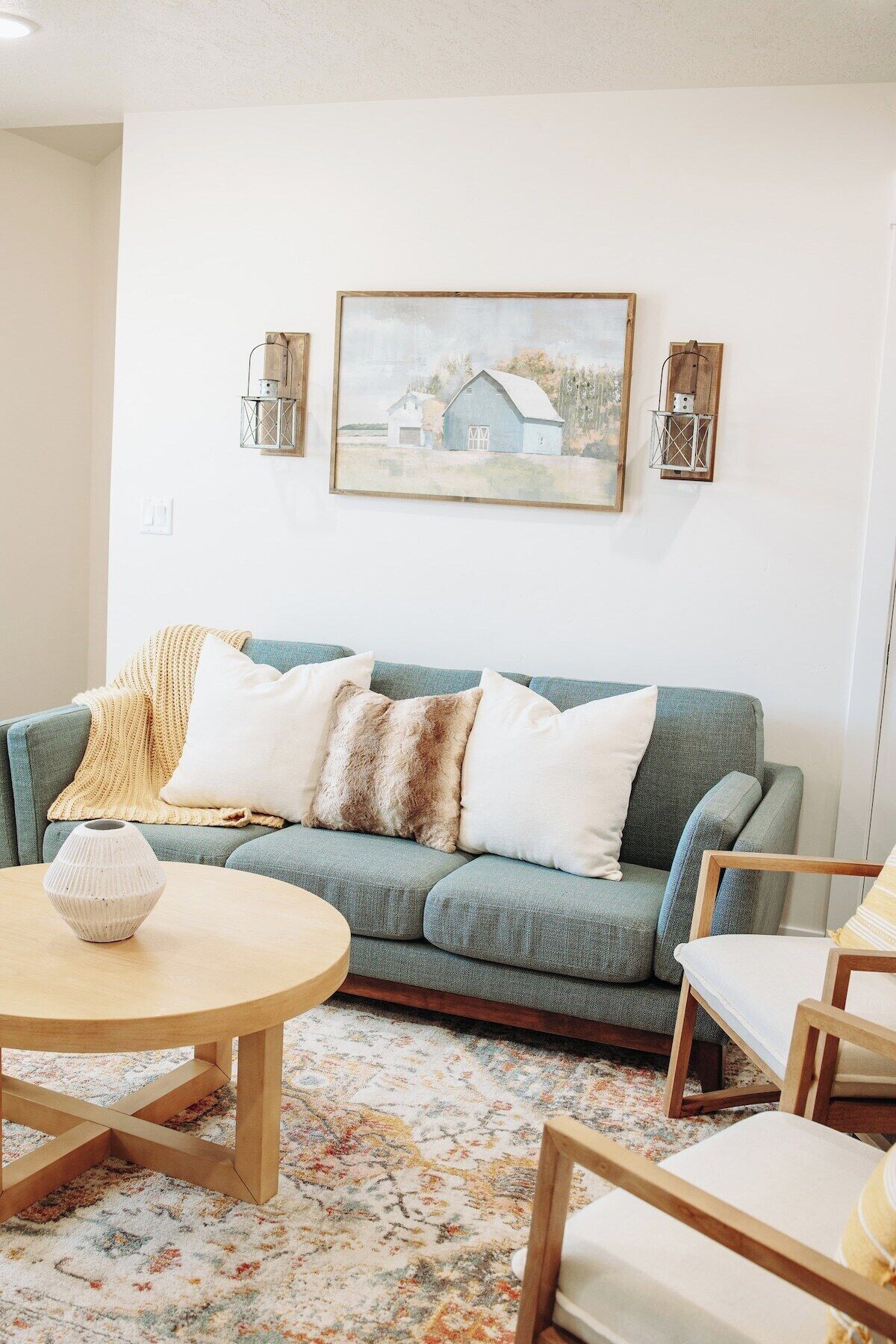 Ein Wohnzimmer mit einem grünen Sofa, einem runden Couchtisch und einem Gemälde einer Scheune an der Wand.