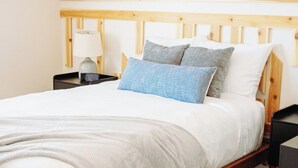 Una cama individual con cabecera de madera, una mesita de noche con lámpara y un reloj digital.
