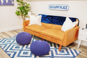 Un salón con un sofá, dos otomanas, una alfombra, una planta, un reloj y un cartel que dice 'OUR HAPPY PLACE'.