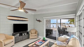 A living room with a TV, seating, a ceiling fan, and a view through a glass door to an outdoor area. - P15 - Waterfront, ground level duplex with Cabana Club (Key Colony Beach)