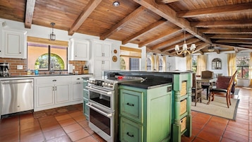 Una cocina con armarios blancos, estufa verde y techo de madera.