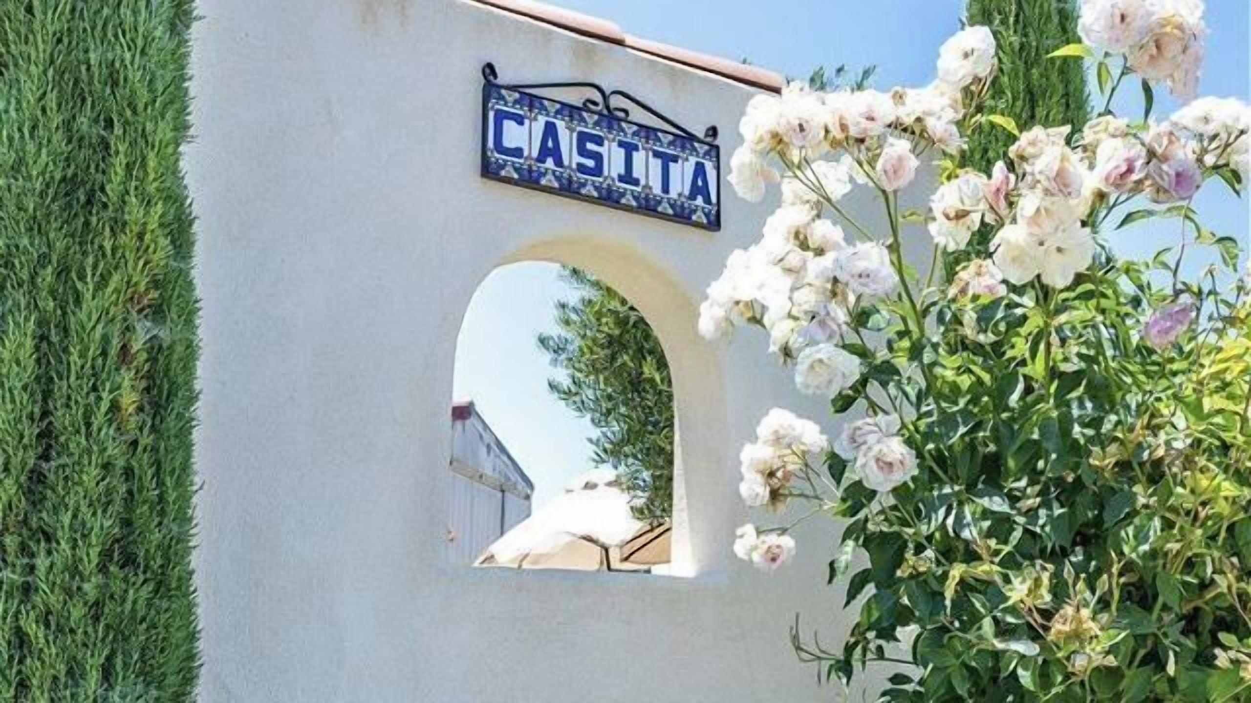 A white wall with a blue sign reading 'CASITA' above an arched window.