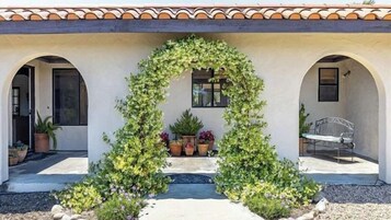Un edificio con un patio cubierto, plantas en macetas y un banco.