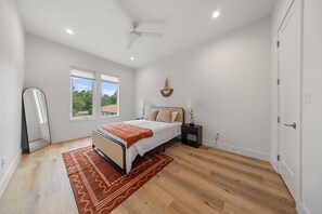 Ein Schlafzimmer mit Bett, Nachttischlampen, Deckenventilator und Blick ins Freie.