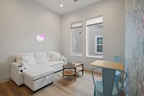 A modern living room with a sectional sofa, a glass coffee table, and a small table with chairs. - Modern Trinity Groves Home w/ Rooftop + Garage (Dallas)