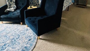 A room with a bed, two chairs, a bedside table with a lamp, and a patterned rug. - Coastal  Serenity 3-bedroom house with heated pool and hot tub (Gulfport)