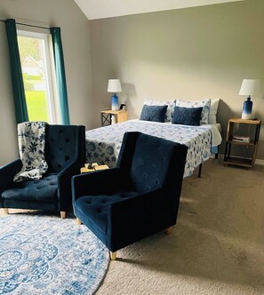 A room with a bed, two chairs, a bedside table with a lamp, and a patterned rug. - Coastal  Serenity 3-bedroom house with heated pool and hot tub (Gulfport)