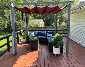 A wooden deck with a covered seating area, a sofa, and potted plants. - Coastal  Serenity 3-bedroom house with heated pool and hot tub (Gulfport)
