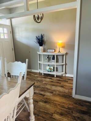 A room with a wooden dining table, white chairs, a white console table with a lamp, and a wall-mounted chandelier. - Coastal  Serenity 3-bedroom house with heated pool and hot tub (Gulfport)