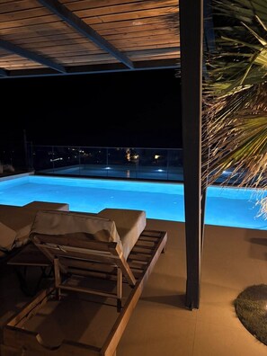 A covered outdoor area with a pool, lounge chairs, and a palm tree. - Stone horizon villa (Myrthianos Plakias)