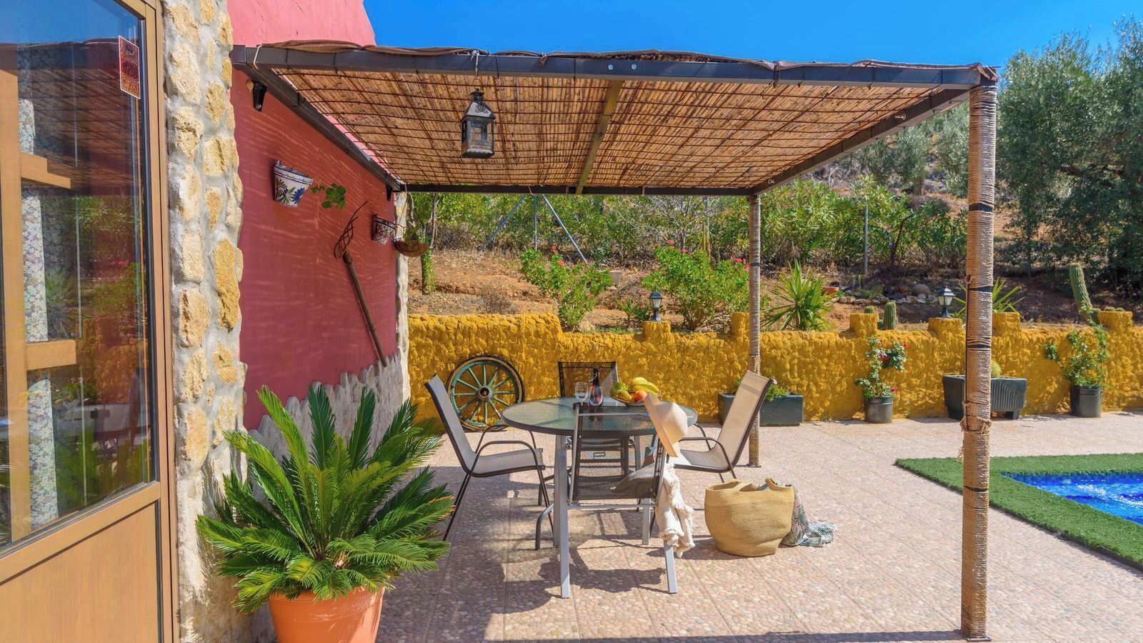 A covered patio area with a table and chairs, a potted plant, and a yellow wall.