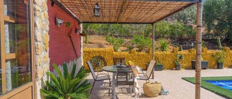 Un patio techado con una mesa, sillas, una planta en maceta y una pared amarilla.