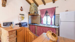 Een keuken met een stenen muur, een houten tafel, een magnetron, een broodrooster, een spoelbak en een koelkast.