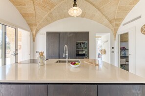 Une cuisine moderne dotée d’un grand îlot central, de meubles de couleur sombre et d’un plafond en pierre.